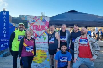 A group of happy and excited people, running the Leicester 10k Run for All in support of Trade, stand in front of a promotional banner.