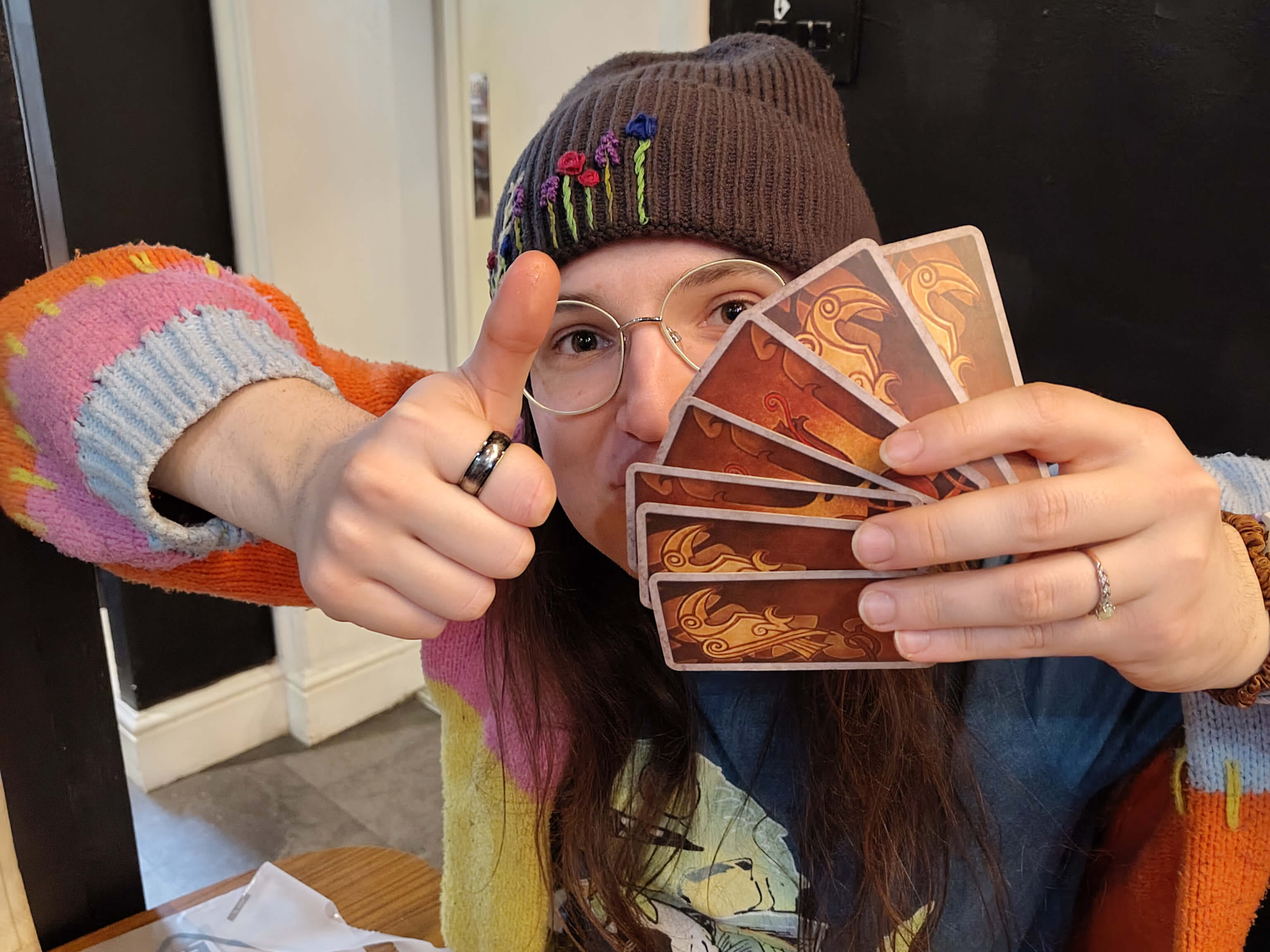 A person giving a thumbs up holds their gaming cards in front of their face.