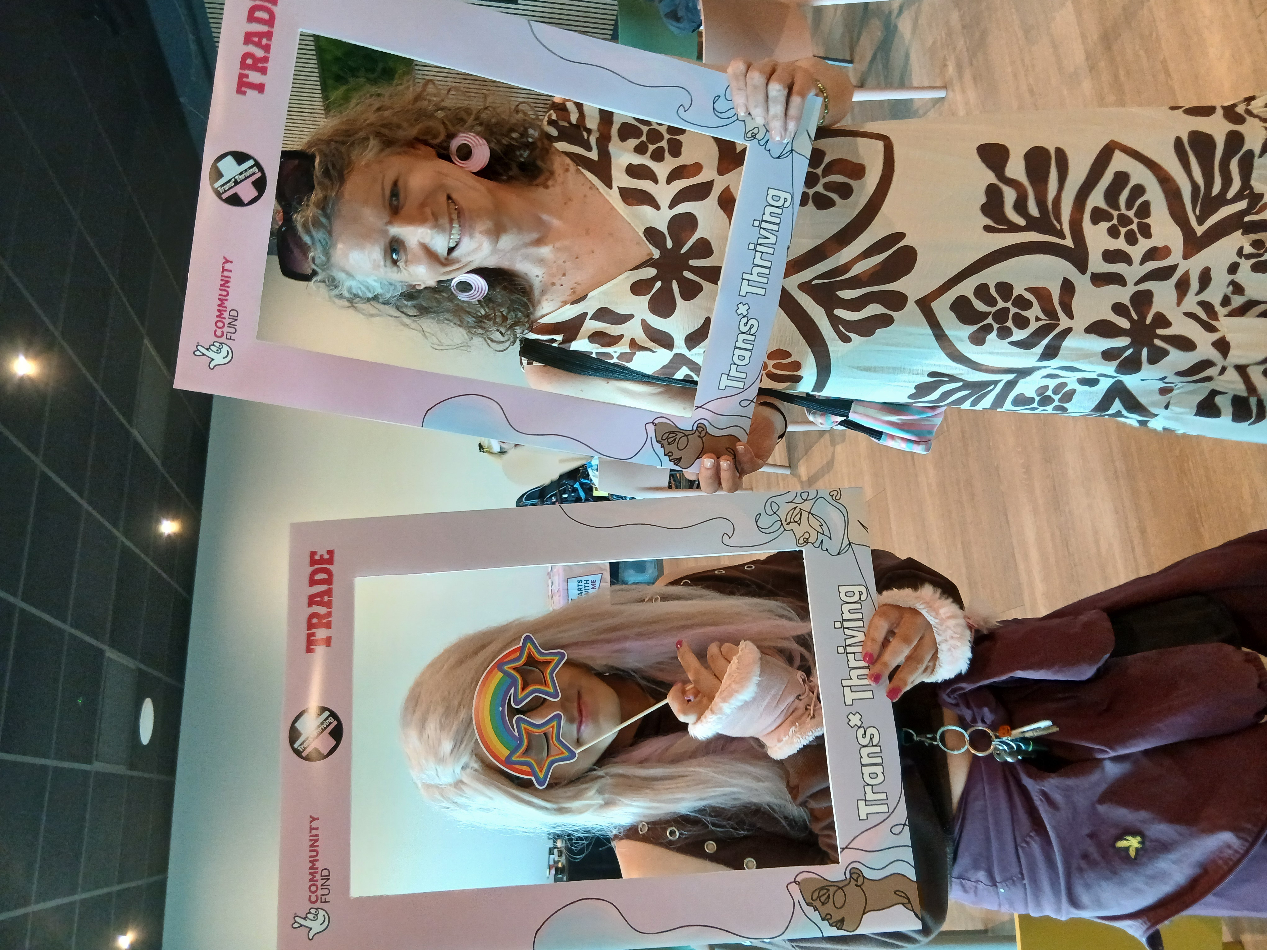 Two people pose with Trans* Thriving selfie frames.